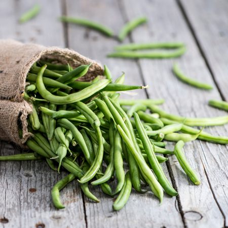 Fresh green beans spilling from a hessian sack onto a wooden table