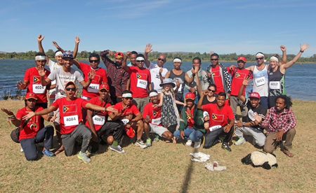 A large group of Ceres Farm seasonal workers in red race shirts posing beside the water at the Kununurra Half Marathon