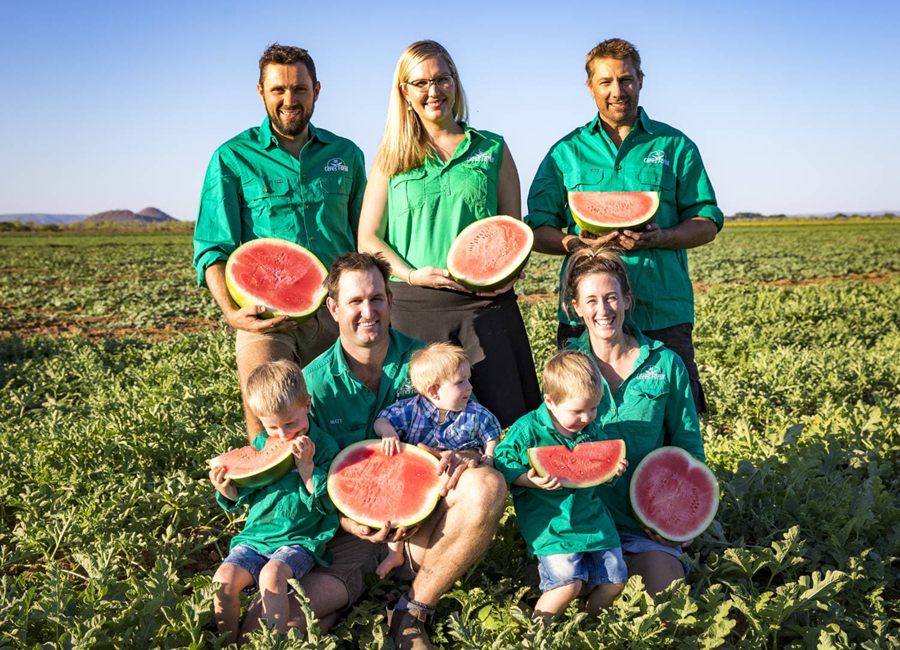 The Gray family and Ceres Farm team holding halved watermelons in a melon field at Ceres Farm