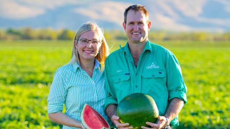 Melanie and Matthew Gray holding a watermelon in a melon field with the Kimberley ranges behind